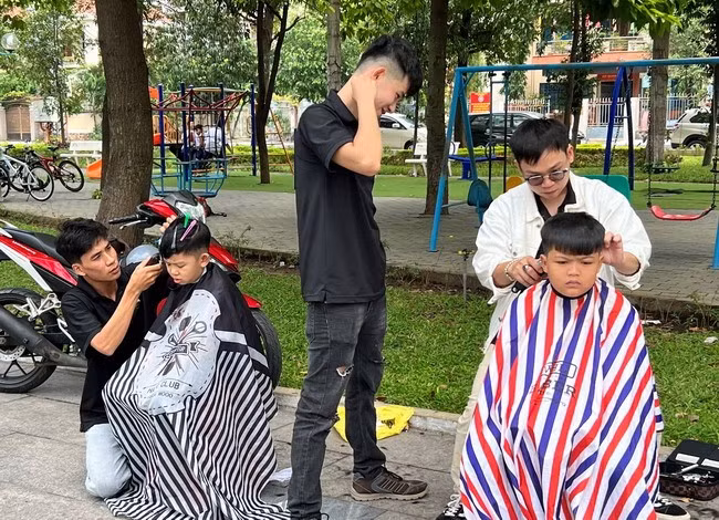 Anh Huỳnh Tấn Phát (giữa) hướng dẫn cho thợ và học viên cắt tóc cho khách hàng “nhí” tại Công viên trung tâm TP Quy Nhơn. Ảnh: D.Đ