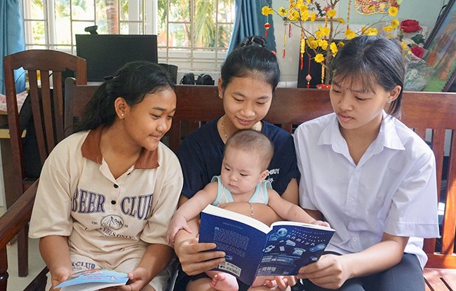 Các em gái ở nhà Hoa Hướng Dương vừa đọc sách vừa trông em giúp mẹ. Ảnh: T.K Các em gái ở nhà Hoa Hướng Dương vừa đọc sách vừa trông em giúp mẹ. Ảnh: T.K