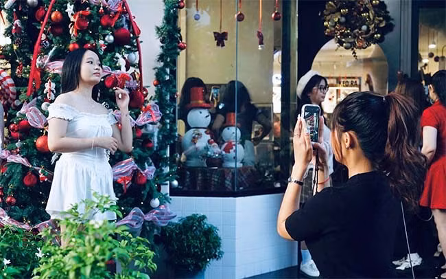 Các bạn nữ “lên đồ” lộng lẫy đang thả dáng chụp ảnh check-in bên cây thông Noel. Ảnh: TN