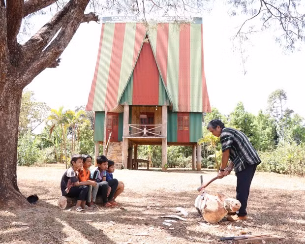 Nghệ nhân ưu tú Ksor Krôh hướng dẫn các em nhỏ tạc tượng gỗ. (Ảnh: Hồng Điệp/TTXVN)