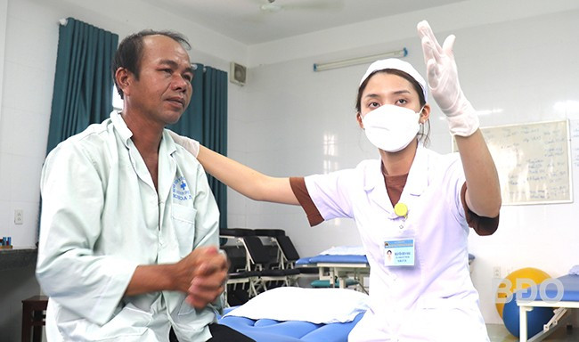 Bệnh nhân Lê Luôn cần mẫn từng chút tập phản xạ và các vận động tay, chân theo hướng dẫn của kỹ thuật viên Nguyễn Bích Hậu. Ảnh: M.H