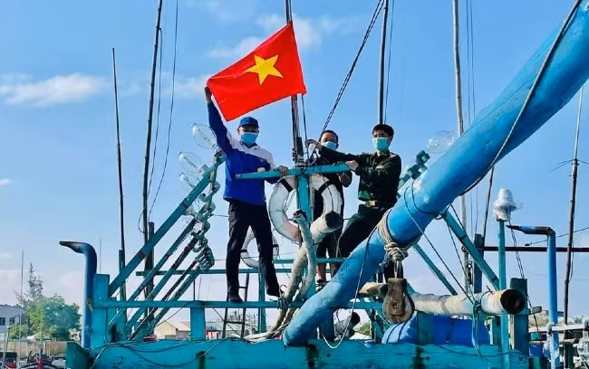 Bộ đội biên phòng tặng và cùng treo cờ Tổ quốc trên tàu cá đánh bắt xa bờ của ngư dân Hoài Nhơn. Ảnh: THANH BÌNH
