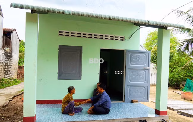 Bà Nguyễn Thị Ba đón người bạn hàng xóm và đại diện chính quyền địa phương trong căn nhà nhỏ nhưng vững vàng, thoáng mát được hỗ trợ sửa chữa từ chương trình xóa nhà tạm, nhà dột nát. Ảnh: NGUYỄN MUỘI