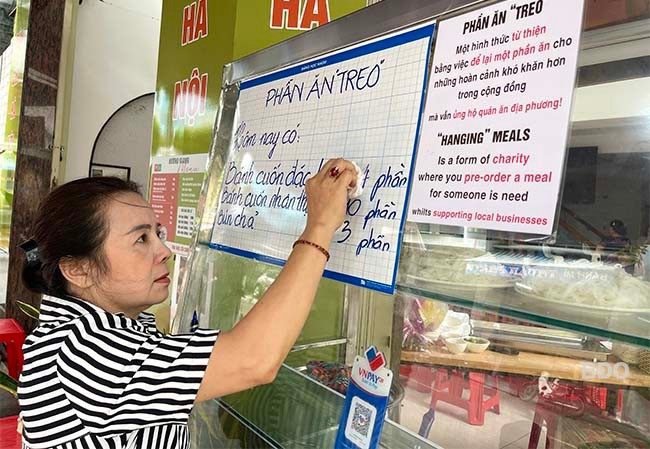 Bà Đào Hương Giang, chủ quán bún chả, bánh cuốn ở 125 Hai Bà Trưng, điền số lượng “treo” lên bảng cho người khó khăn đến ăn. Ảnh: HẢI YẾN