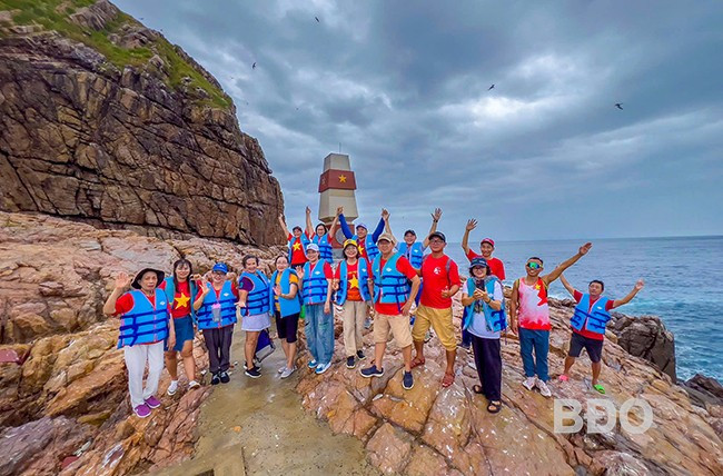 Anh Nguyễn Hữu Đảo (hàng đầu, thứ hai từ phải sang) dẫn du khách trải nghiệm cột mốc A9 trên biển tại hòn Ông Căn ở xã Nhơn Lý. Ảnh: NVCC