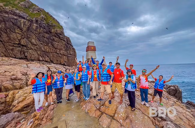 Anh Nguyễn Hữu Đảo (hàng đầu, thứ hai từ phải sang) dẫn du khách trải nghiệm cột mốc A9 trên biển tại hòn Ông Căn ở xã Nhơn Lý. Ảnh: NVCC