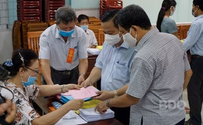 Đồng chí Nguyễn Tuấn Thanh cùng các cử tri nhận phiếu bầu cử. ẢNH: KIỀU ANH