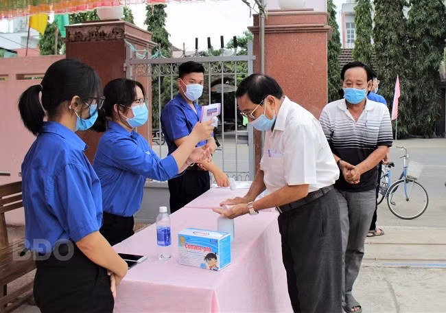 Đoàn viên thanh niên đo thân nhiệt và nhắc cử tri khử khuẩn trước khi vào khu vực bầu cử. ẢNH: NGUYỄN MUỘI