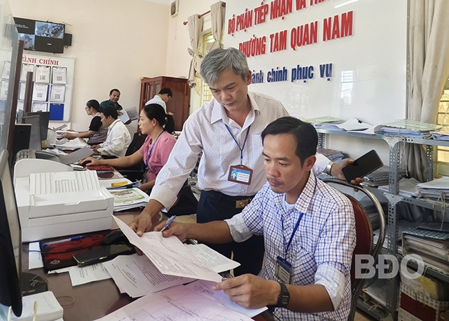 Công chức Nguyễn Thành Trung (người đứng) trao đổi công việc với đồng nghiệp. Ảnh: H.THU