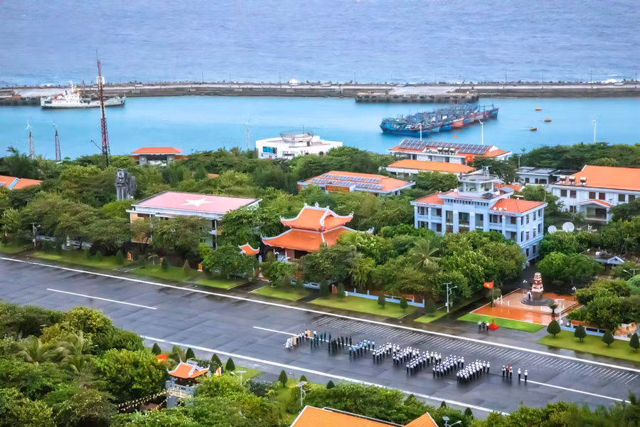 Quân và dân đặc khu Trường Sa thực hiện nghi lễ chào cờ đầu tuần, trên đường băng sân bay Trường Sa, phía sau là âu tàu