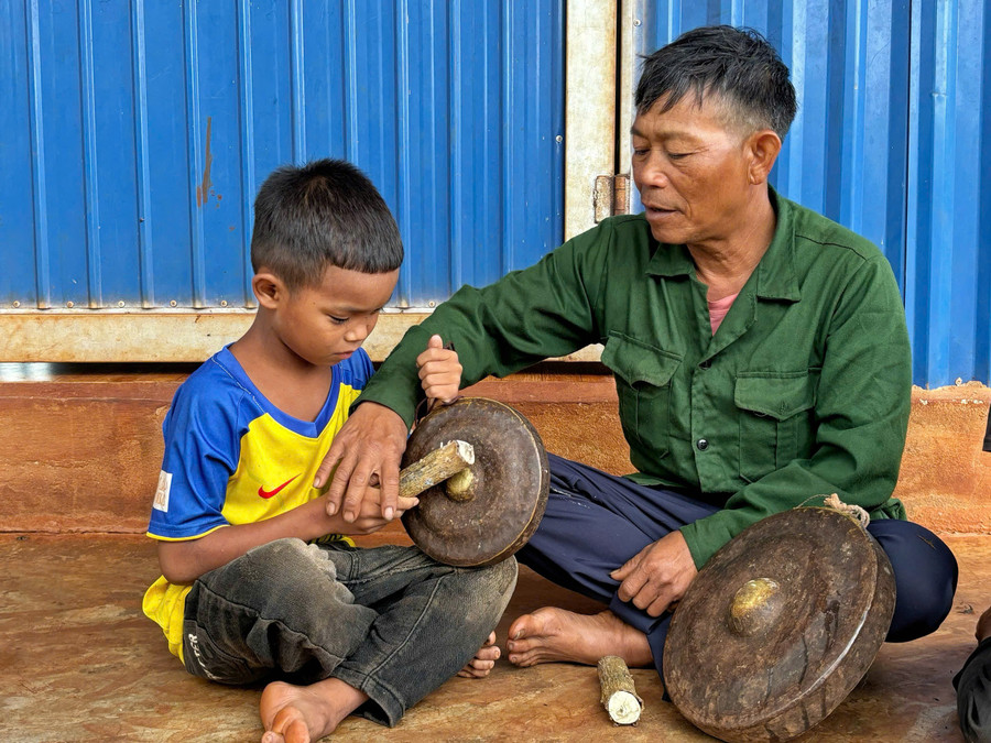 Ông Mlang đang hướng dẫn em Anh đánh chiêng. Ảnh: Đồng Lai ong-mlang-ben-phai-dang-huong-dan-em-anh-ben-trai-dang-chieng-anh-dong-lai.jpg