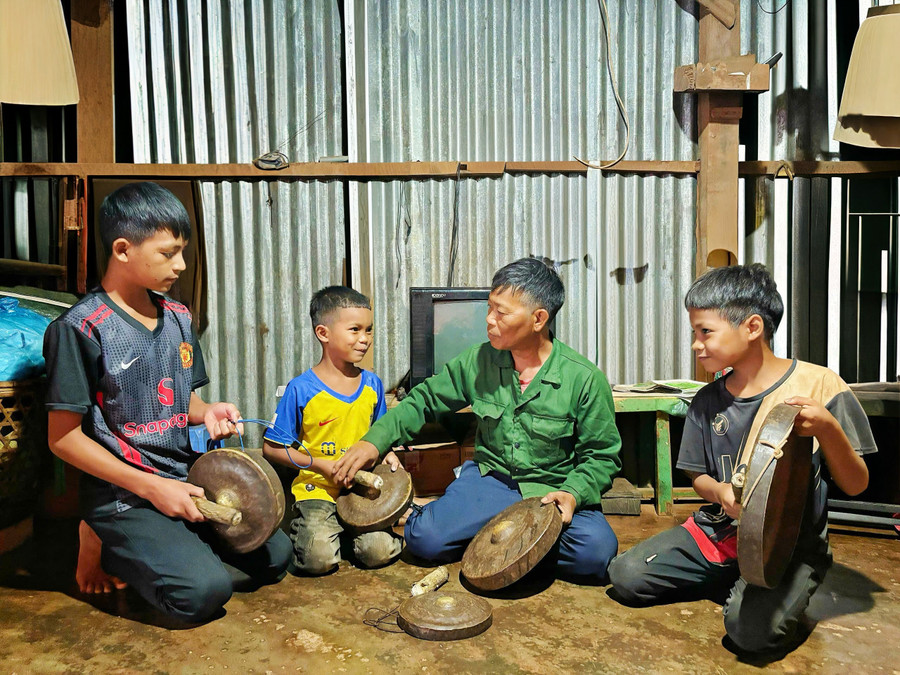 Ông Mlang (áo xanh) hướng dẫn nhóm trẻ em làng Kol đánh cồng chiêng tại nhà. Ảnh: Đồng Lai ong-mlang-ao-xanh-huong-dan-nhom-tre-em-lang-kol-danh-cong-chieng-tai-nha-anh-dong-lai.jpg
