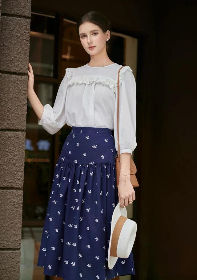 Chân váy xanh điểm hoa trắng phối áo kiểu màu trắng viền ren, tay lỡ điệu đà giúp nàng thăng hạng nhan sắc nơi công sở mùa hè