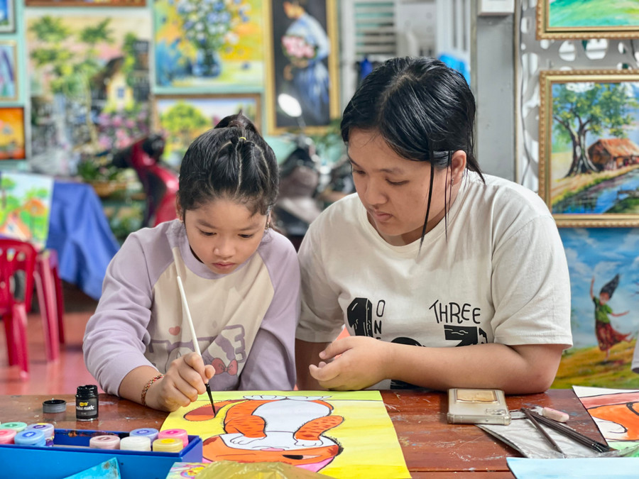 Bạn Cao Võ Gia Hân hỗ trợ thầy Thành hướng dẫn cho các em tại lớp học vẽ. Ảnh: Bích Ngọc