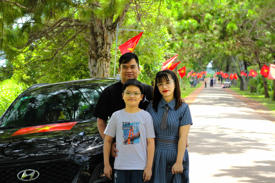 Gia đình chị Trương Thị Tuyết Bông (tổ 8, phường Yên Thế, TP. Pleiku) check in với chiếc xe dán lá cờ Tổ quốc tại con đường hàng thông trăm tuổi, xã Nghĩa Hưng, huyện Chư Păh. Ảnh: Hoàng Hoài