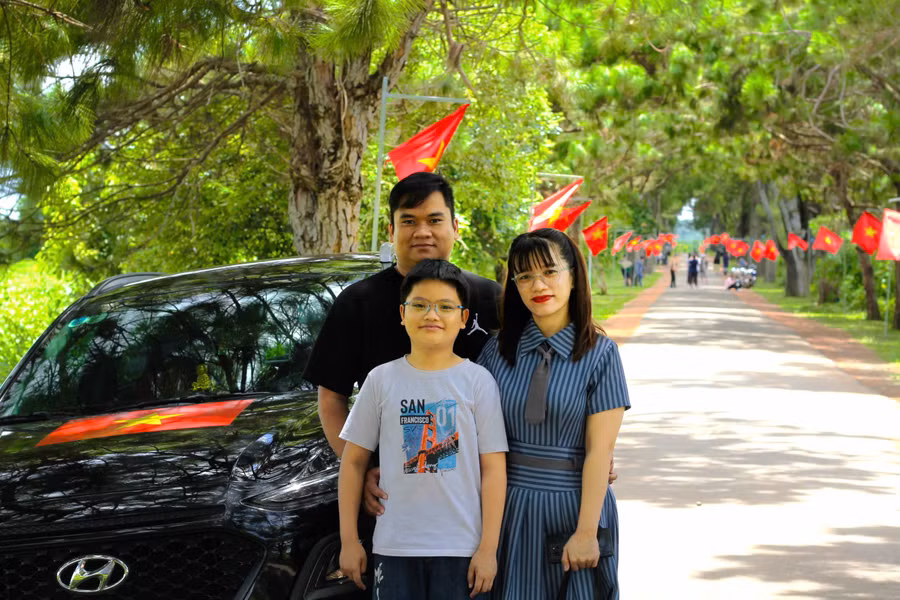 Gia đình chị Trương Thị Tuyết Bông (tổ 8, phường Yên Thế, TP. Pleiku) check in với chiếc xe dán lá cờ Tổ quốc tại con đường hàng thông trăm tuổi, xã Nghĩa Hưng, huyện Chư Păh. Ảnh: Hoàng Hoài