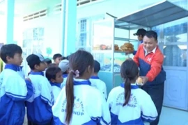 Thầy giáo Vũ Văn Tùng(mặc áo đỏ xanh) đang hỗ trợ bánh mì cho học sinh Trường Tiểu học và THCS Đinh Núp(ở xã Pơ Tó, huyện Ia Pa, tỉnh Gia Lai). * ảnh: Hoàng Cư