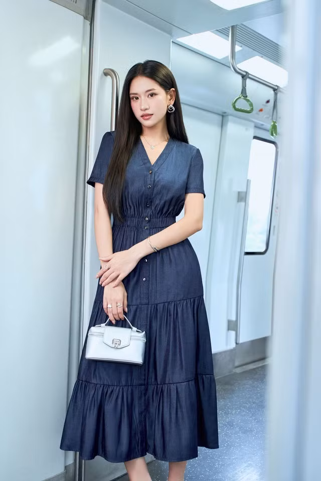 Thiết kế váy denim xếp tầng bồng bềnh duyên dáng với phần eo bo nhẹ tôn vòng eo thon gọn, cổ chữ V cùng hàng nút trước tạo điểm nhấn thanh lịch và hiện đại. Chất liệu denim mềm giúp váy giữ phom tốt nhưng vẫn thoải mái, dễ chịu trong mùa nắng