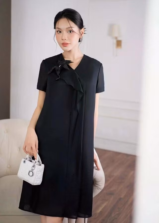 Thiết kế suông tinh giản nhưng sang trọng gam màu đen phù hợp với nhiều dáng người, vừa có thể giấu nhược điểm hình thể vừa giữ trọn nét thanh thoát. Chi tiết cổ chữ V đính hoa bên cạnh đường bèo nhẹ nhàng, tô điểm nét mềm mại nữ tính của quý cô