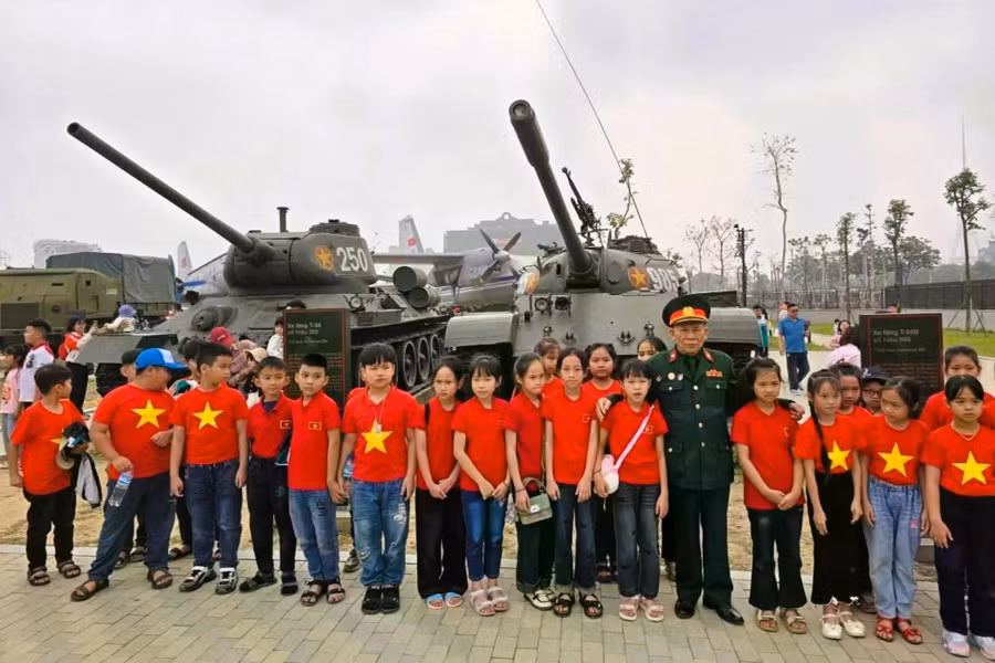 Cựu chiến binh tăng thiết giáp và các em học sinh chụp hình lưu niệm trước hiện vật xe tăng, trưng bày tại Bảo tàng Lịch sử Quân sự Việt Nam. Ảnh: Huy Nguyễn
