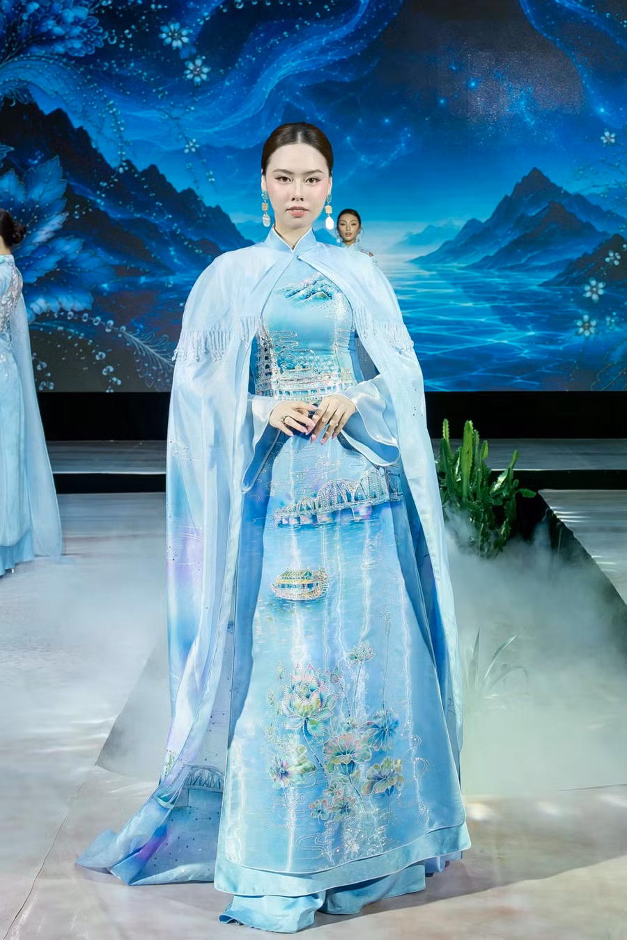 Đặng Hoàng Tâm Như duyên dáng trong tà áo dài xanh với hình ảnh hoa sen và các họa tiết quen thuộc với vùng đất cố đô. Điểm nhấn của bộ trang phục là chi tiết áo choàng cầu kỳ phía sau, giúp toát lên vẻ nữ tính của người mặc