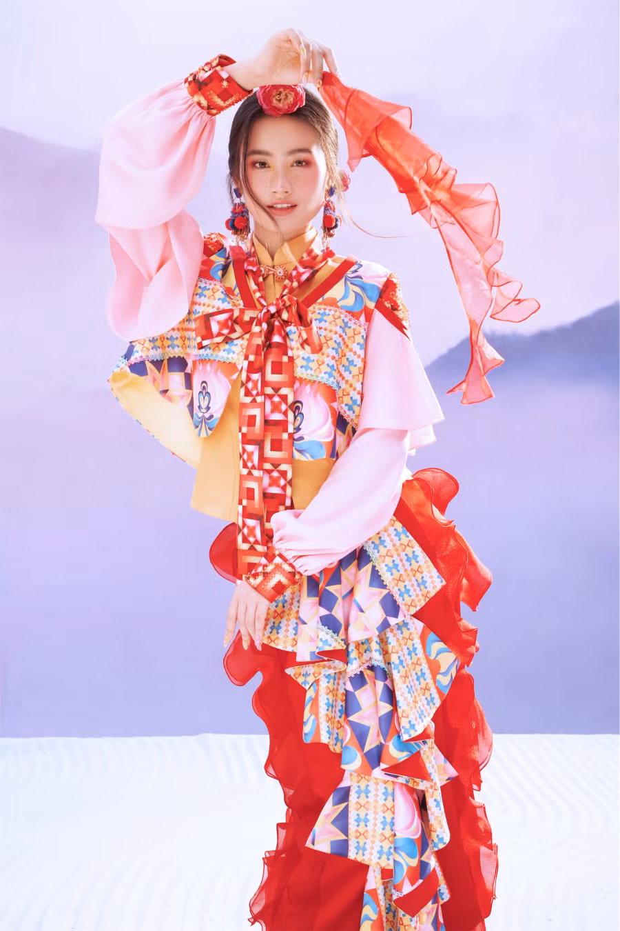 Những ô màu hình thoi trên bản vẽ tưởng chừng đặt để ngẫu nhiên, nhưng lại có những hàng, lớp và quy luật nhất định, đảm bảo được tính cân bằng chủ đạo trong trang trí hoa văn trên chiếc khăn biểu tượng. Khi diện trang phục với họa tiết lạ mắt, Ý Nhi còn kết hợp cùng vòng cổ, hoa tai, búi tóc đồng điệu