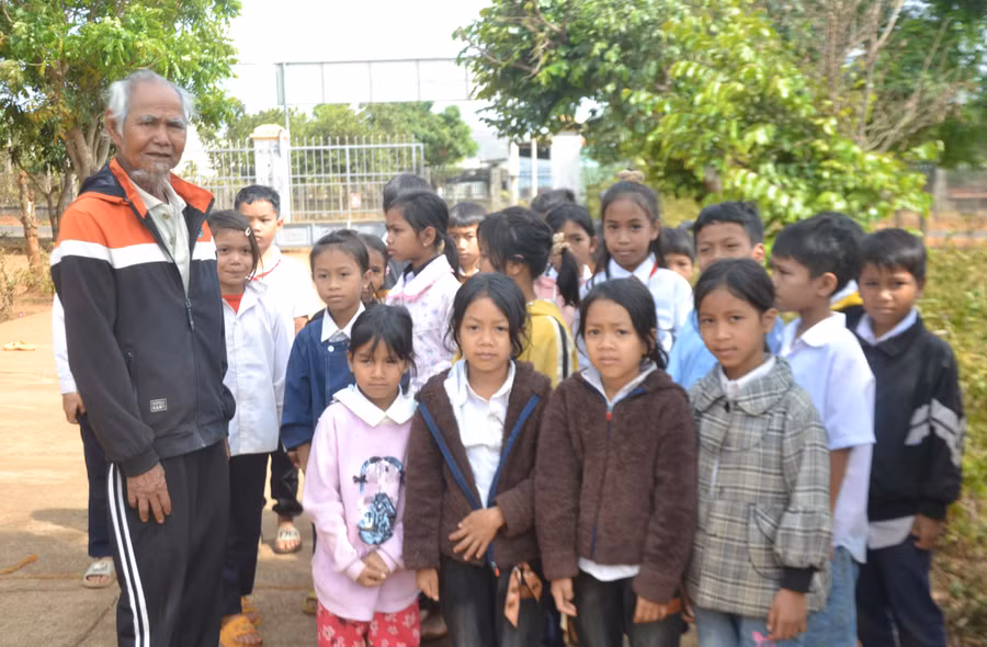 Ông Han (bên trái) tuyên truyền, vận động các cháu thiếu nhi ở làng Chăm Nek đi học chuyên cần. Ảnh: H.M