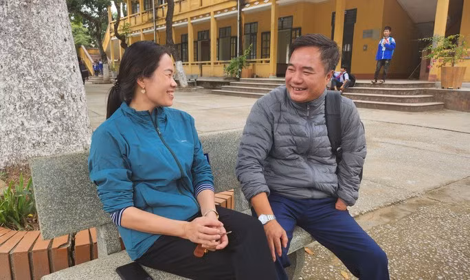 Vợ chồng thầy Hương trò chuyện dưới sân trường trong giờ giải lao.