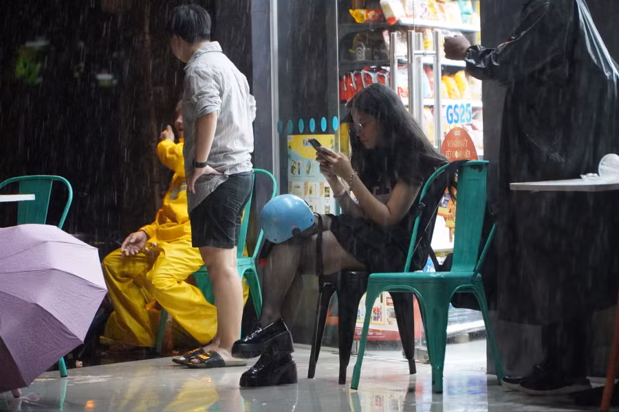 Người dân núp mưa, tránh ngập trước hiên nhà ven đường.