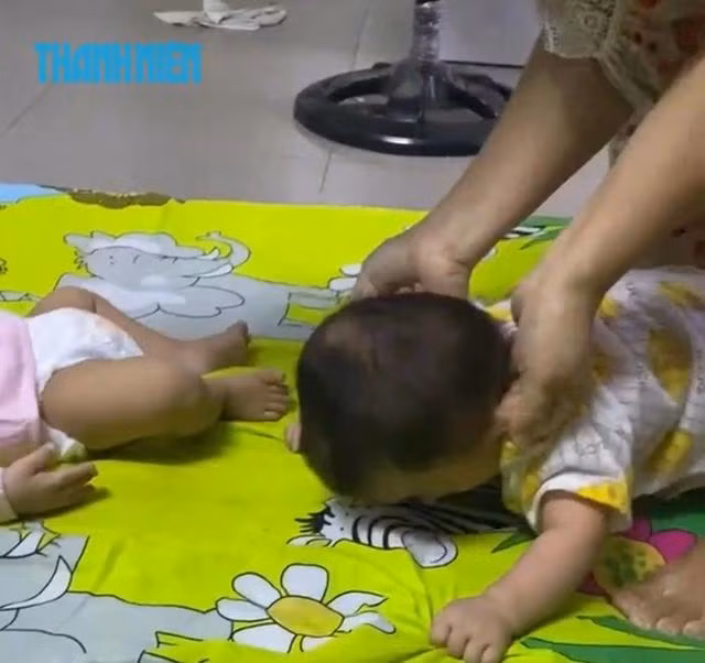 Bé trai (7 tháng tuổi) bị bà Tuyền ngồi lên người, nhéo lỗ tai, bạo hành dã man. Em bé đau đớn, hai tay nắm chặt tấm nệm