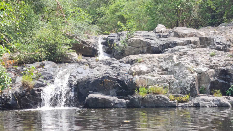 Nhìn ra xa, dòng nước trong veo len lõi trong những tảng đá lớn nhỏ từ phía trên chảy xuống giữa núi rừng xanh ngát.