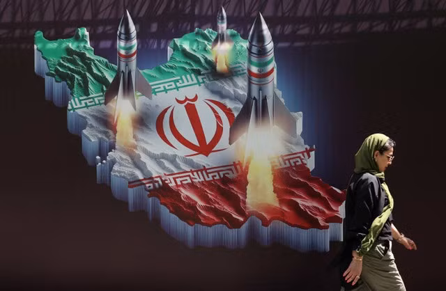 Một phụ nữ Iran đi ngang qua biểu ngữ chống Israel có hình ảnh tên lửa Iran trên đường phố ở Tehran. Ảnh: Reuters