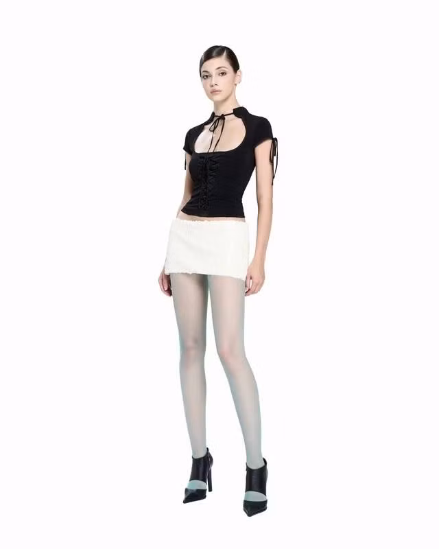 Mang vẻ cổ điển pha trộn tinh thần gothic hiện đại, áo đen ôm sát, khoét ngực sâu, kết hợp chi tiết nơ cổ thanh mảnh và corset dây rút. Chiếc chân váy trắng siêu ngắn đóng vai trò như một mảng sáng nổi bật, tôn lên đôi chân dài và đường nét thanh thoát của tổng thể. ẢNH: LSOUL