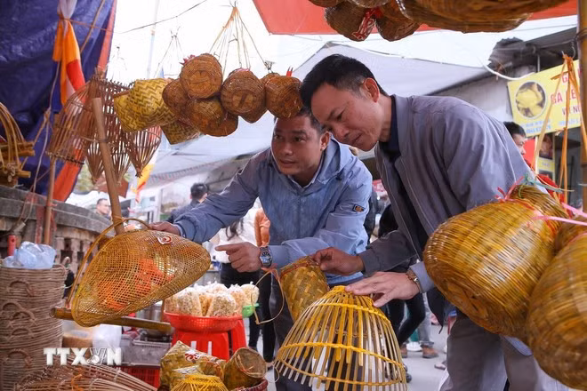 Du khách tham quan, lựa chọn mua những kỷ vật nghề nông để lấy may mắn khi đi chợ Viềng. (Ảnh: Công Luật/TTXVN)