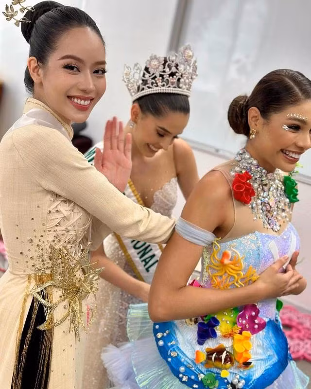 Andrea Rubio và Thanh Thủy giúp đỡ một thí sinh khác trong buổi trình diễn trang phục dân tộc. ẢNH: MISS INTERNATIONAL