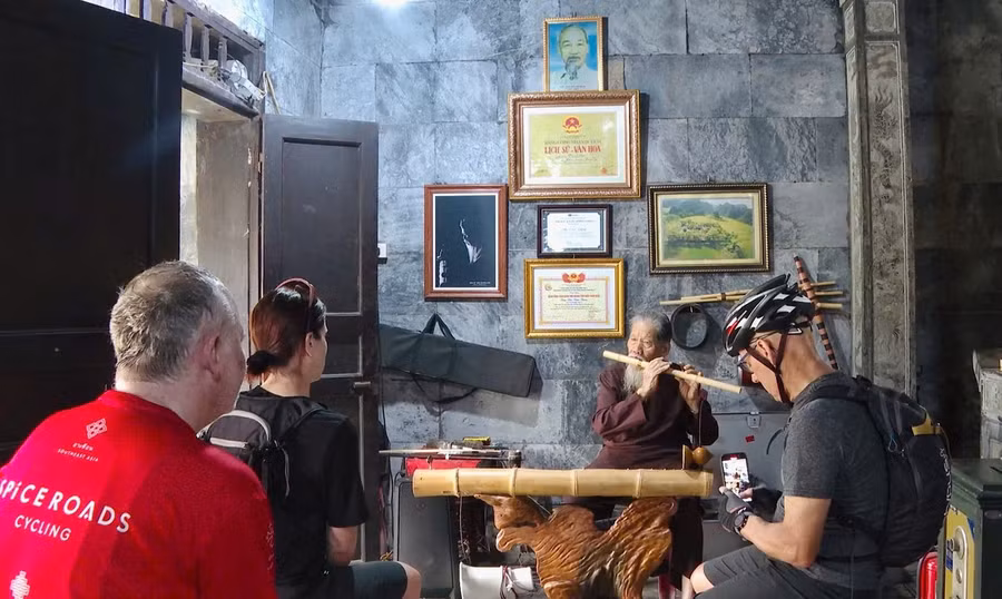 Du khách quốc tế đến thăm đền Thái Vi thích thú ghi lại hình ảnh cụ Thim biểu diễn âm nhạc dân tộc, sử dụng nhiều loại nhạc cụ truyền thống. Ảnh: Đình Minh