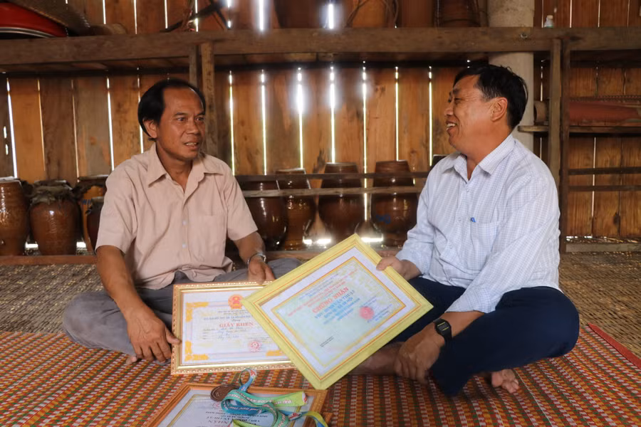 Ông Đinh Văn Nhin (bìa trái) tự hào kể về những thành tích gia đình đạt được trong môn thi chạy cà kheo với ông Lý Văn Thắng-công chức Văn hóa-Xã hội xã Ya Hội, huyện Đak Pơ. Ảnh: Ngọc Minh