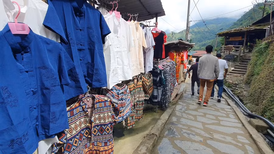 Lối đi xuống bản Cát Cát đầy rẫy những cửa tiệm bán hàng đặc sản, quần áo trang phục theo văn hóa địa phương. Ảnh: KHANG KA Lối đi xuống bản Cát Cát đầy rẫy những cửa tiệm bán hàng đặc sản, quần áo trang phục theo văn hóa địa phương. Ảnh: KHANG KA