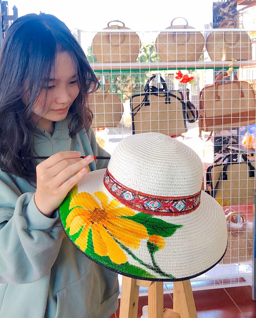 Em Lê Dương Bảo Vy vẽ trang trí hoa dã quỳ và họa tiết thổ cẩm trên chiếc mũ cói thô. Ảnh: Mộc Trà