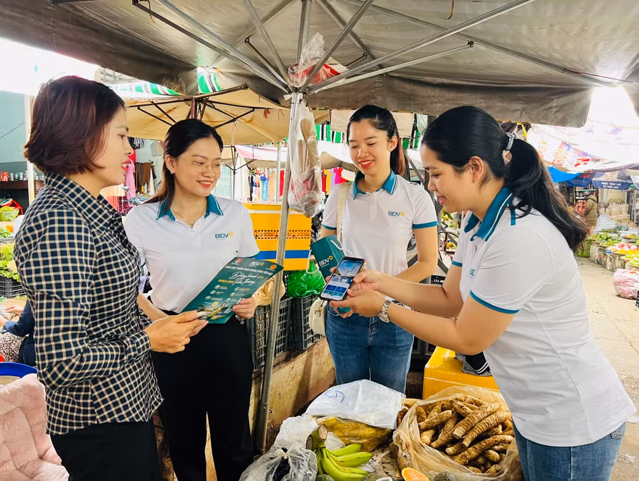 Các thành viên tổ chuyển đổi số hướng dẫn tiểu thương phường Hoa Lư dịch vụ thanh toán không dùng tiền mặt. Ảnh: M.N
