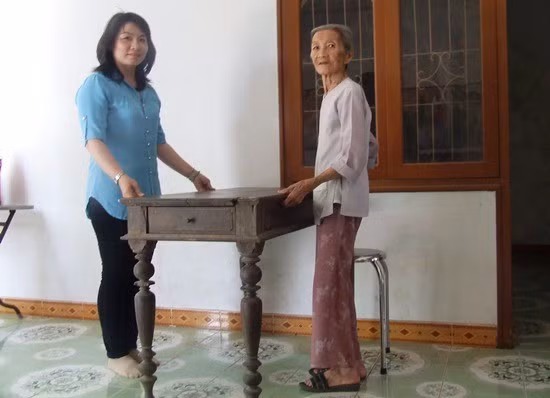 Cán bộ Bảo tàng Tổng hợp tỉnh (bên trái) tiếp nhận kỷ vật chiếc bàn sử dụng vào việc nuôi giấu cán bộ cách mạng thời kháng chiến được một gia đình ở huyện Hoài Nhơn trao tặng.