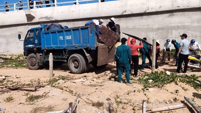 Lực lượng chức năng thu gom các vật liệu dùng để phơi mực tại khu vực kè đầu cầu Đề Gi. Ảnh: N.HÂN