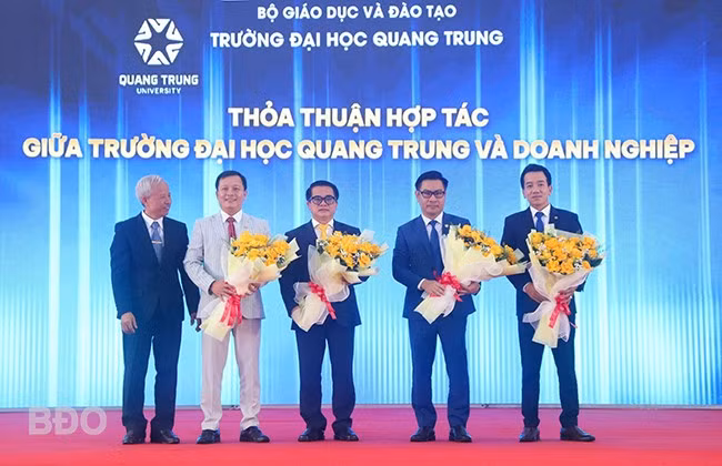 Trường ĐH Quang Trung trao, nhận biên bản ghi nhớ và tặng hoa chúc mừng các DN, đối tác. Ảnh: HỒ ĐIỂM