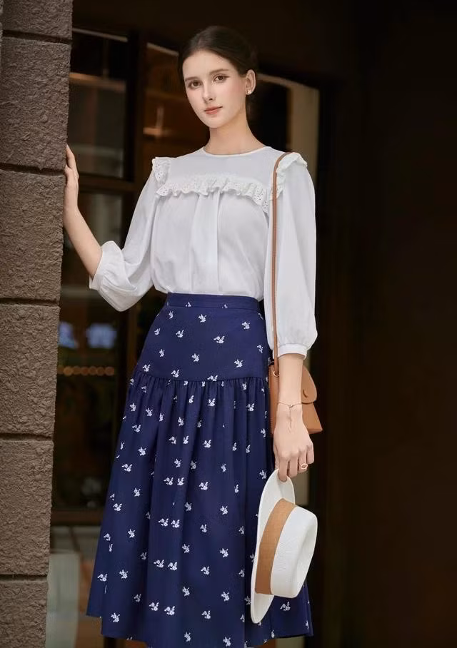 Chân váy xanh điểm hoa trắng phối áo kiểu màu trắng viền ren, tay lỡ điệu đà giúp nàng thăng hạng nhan sắc nơi công sở mùa hè