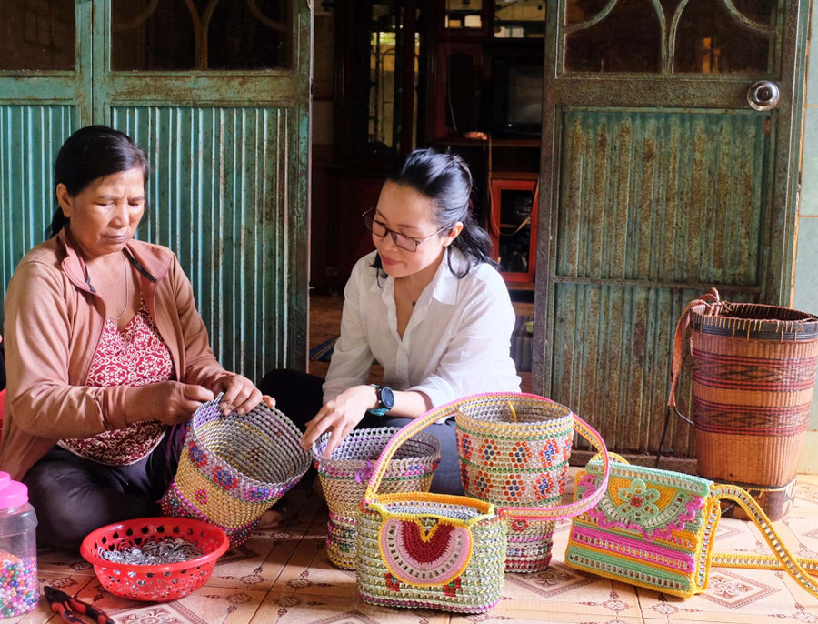 Chị Rơ Mah Vo (bìa trái) giới thiệu các sản phẩm thủ công mỹ nghệ do mình làm với tác giả bài viết. Ảnh: Minh Châu