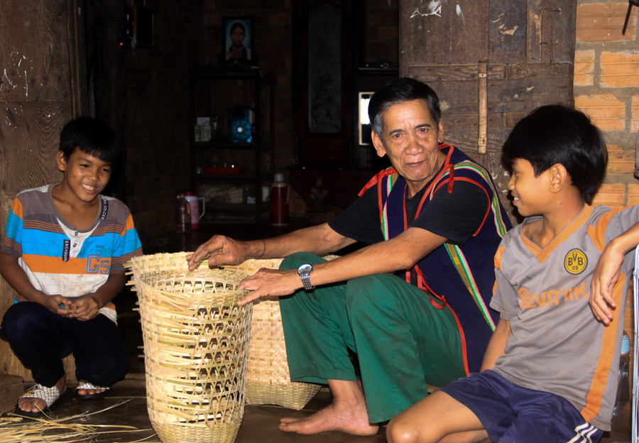 Ông A Dip tranh thủ những lúc đan lát để trò chuyện và dạy dỗ các cháu về văn hóa truyền thống của dân tộc. Ảnh: HT