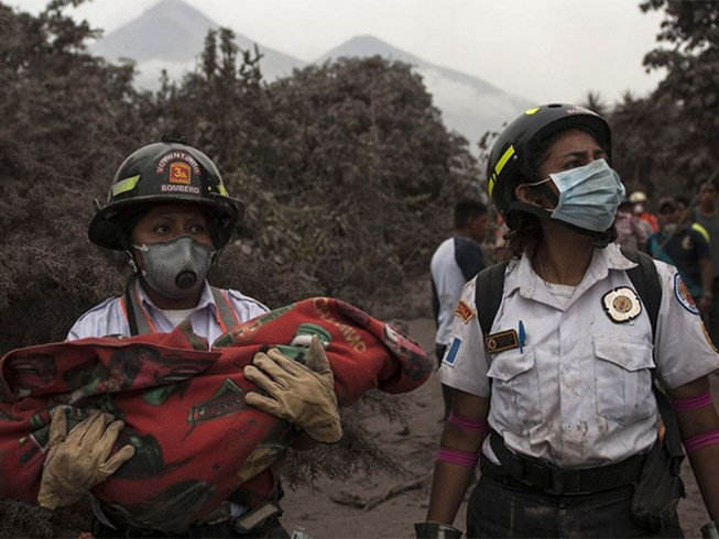 Một lính cứu hỏa bế thi hài trẻ em bị thiệt mạng trong vùng ảnh hưởng của vụ phun trào. Ảnh: AP