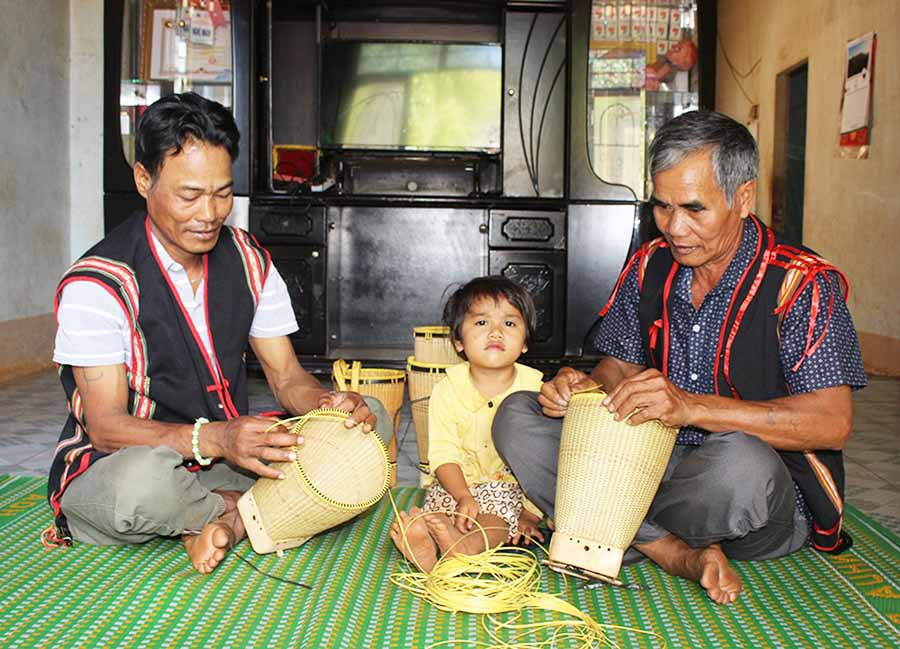Già làng Rơ Lan Hào (bìa phải) là người giỏi đan gùi và sẵn sàng truyền nghề cho những người trẻ trong làng. Ảnh: T.B