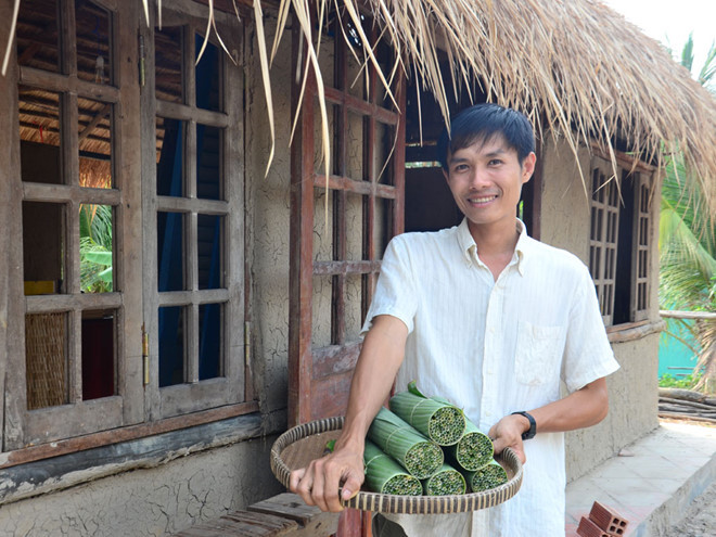 Trần Minh Tiến cầm trên tay sản phẩm ống hút cỏ được gói bằng lá chuối
