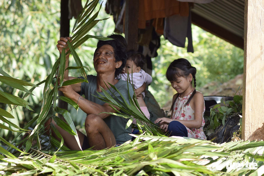 Người đàn ông chuẩn bị lá để thay mái cũ, có cô bé phụ giúp - Ảnh: LÊ VĂN ÁNH